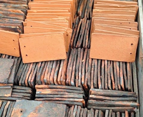 Stacked terracotta and dark clay roof tiles organized in bundles for construction or restoration materials