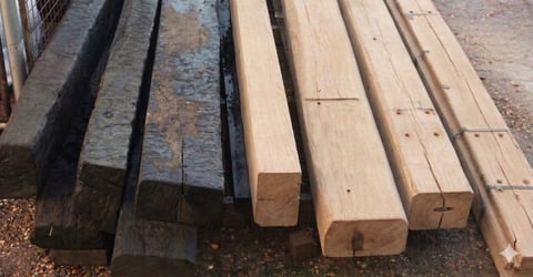 Stack of lumber showing dark treated wood planks on left and natural light-colored wooden beams on right arranged in rows