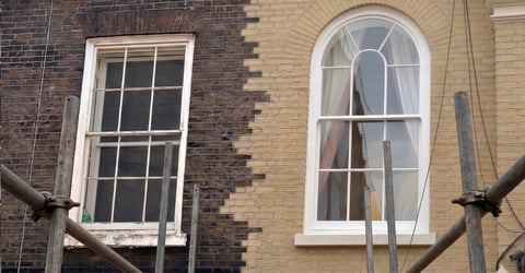 Brick building facade with two white-framed windows and horizontal wooden beams crossing in front
