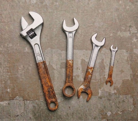 Four adjustable wrenches of decreasing sizes with metal heads and rust-patina copper handles arranged on a concrete surface