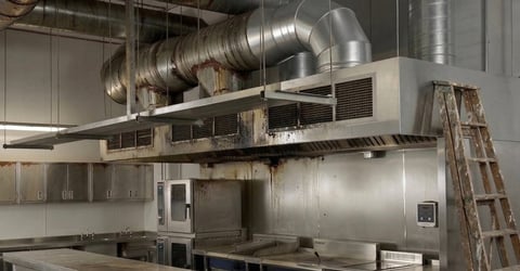 Commercial kitchen with stainless steel hood, ductwork, and equipment installation in progress with ladder visible
