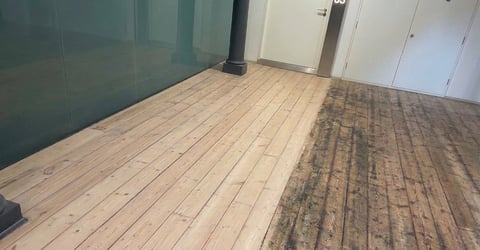 Interior room with partially refinished wood flooring, showing light natural wood on left and stained dark wood on right, with glass partition and white doors
