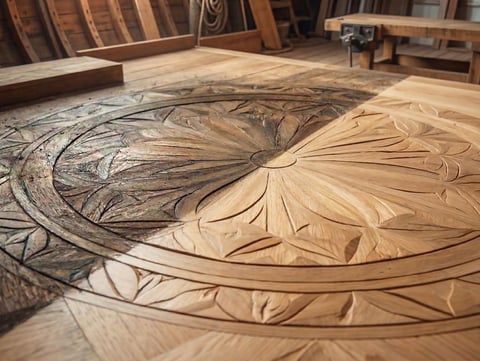 Ornate wooden floor medallion with carved floral and spiral designs in a carpentry workshop