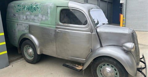 Vintage two-tone cargo van from the 1940s parked in an industrial garage setting with corrugated metal walls