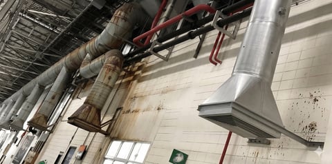 Industrial warehouse interior with exposed ductwork, pipes, and metal ventilation systems mounted on ceiling