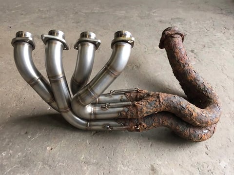 Exhaust manifold with polished stainless steel runners attached to rusted cast iron pipes on concrete surface