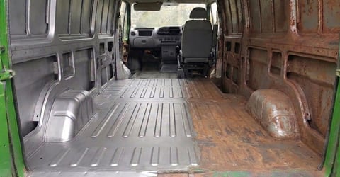 Interior of an empty cargo van with metal ribbed flooring, open rear doors, and front cabin visible