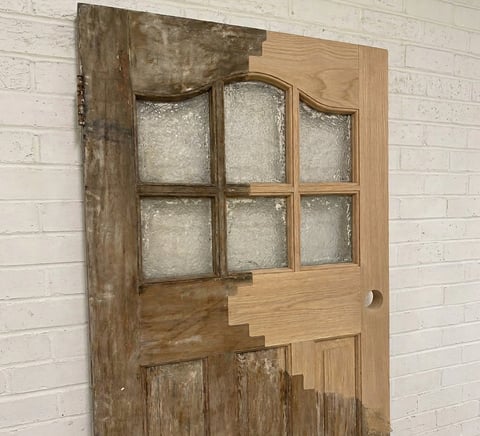 Vintage wooden door with six glass panes on upper half and solid wood panels below, hung on white brick wall