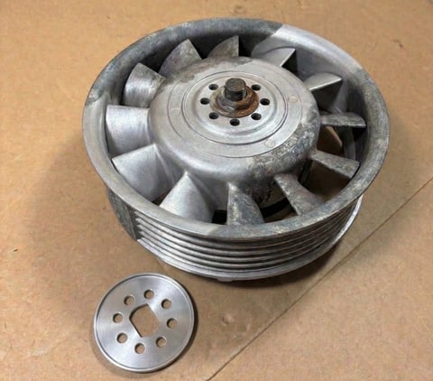 Disassembled aluminum engine pulley showing main component and small separator ring on tan surface