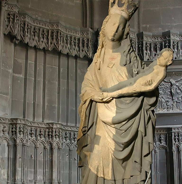 Stone statue of a woman holding a child in front of ornate Gothic architectural details and wooden doors