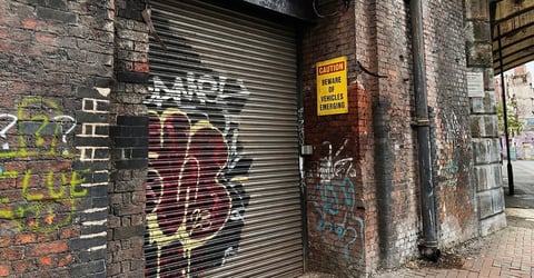 Traditional stone cottage with cream and tan walls, dark roof, red entrance door, and black metal fencing in rural countryside setting