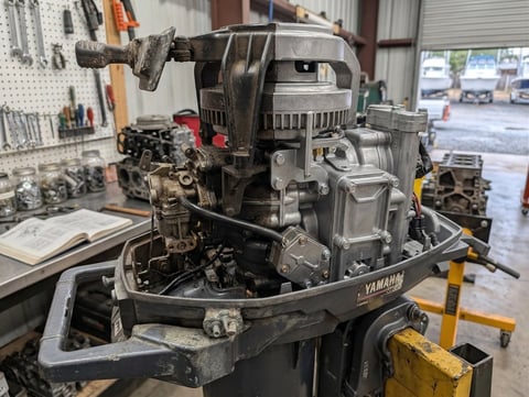 Disassembled Yamaha marine outboard engine on workbench in repair shop with tools visible in background